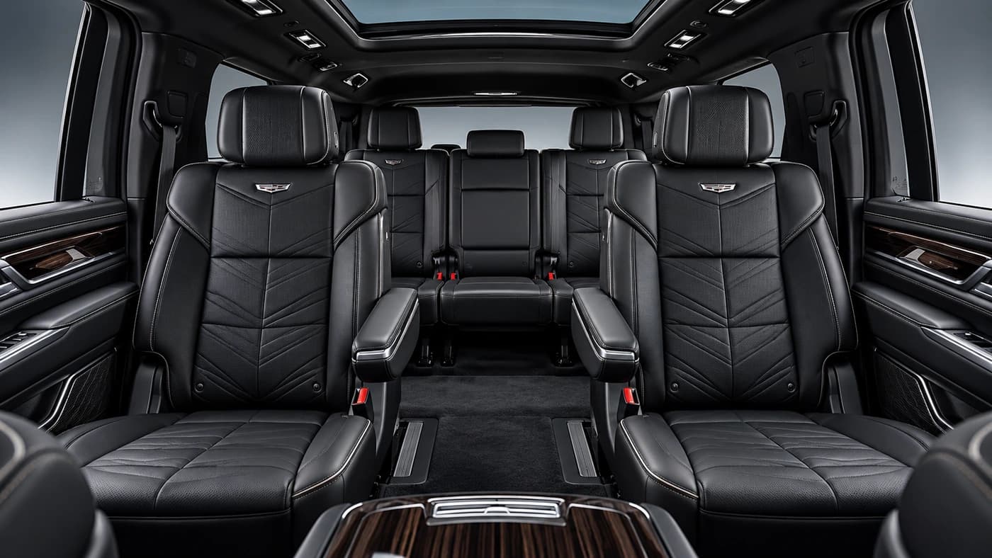 Rear angle of the Cadillac Escalade interior showing black leather seats, diamond stitching, wood trim, and overhead lighting.