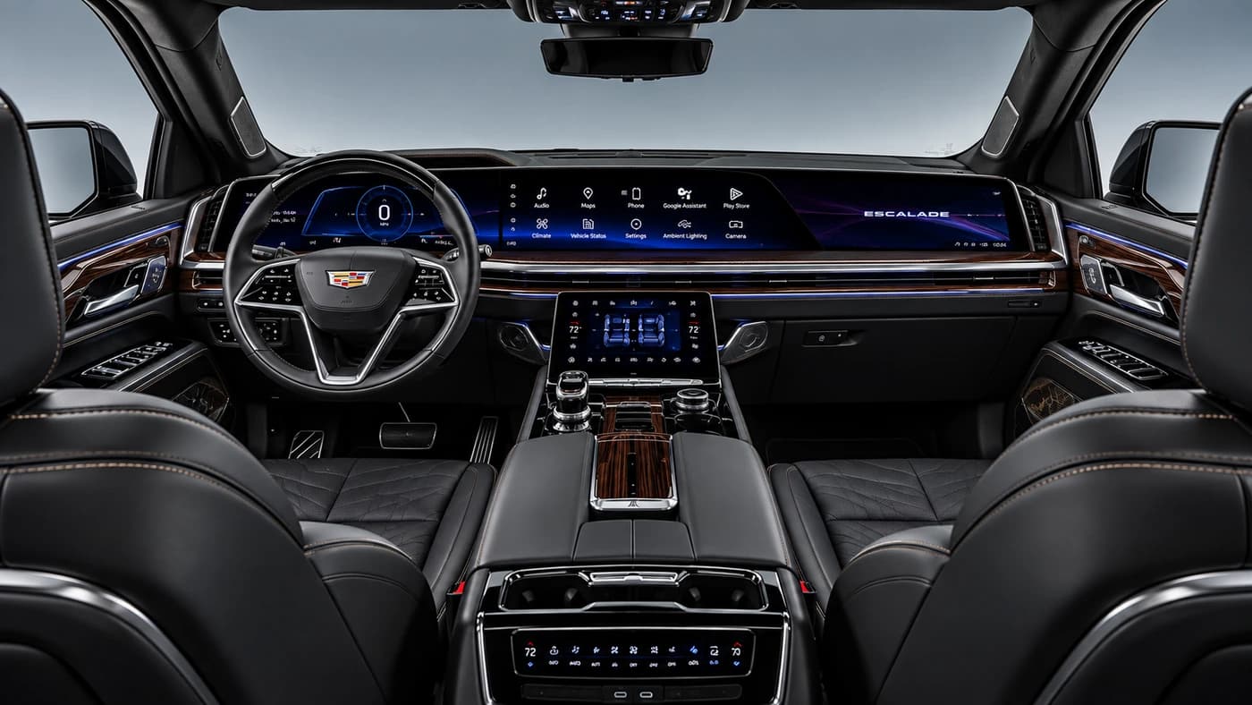 Front view of the Cadillac Escalade interior showing black leather seating, wood trim, digital screens, and ambient lighting.