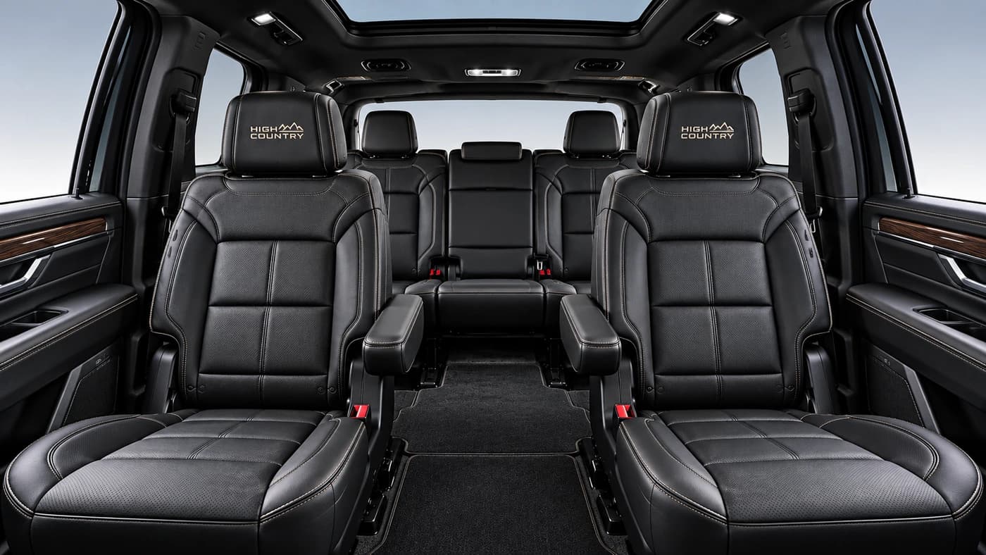 A front-facing angle of the Chevy Suburban interior showing black leather seating, wood trim, and ambient lighting.