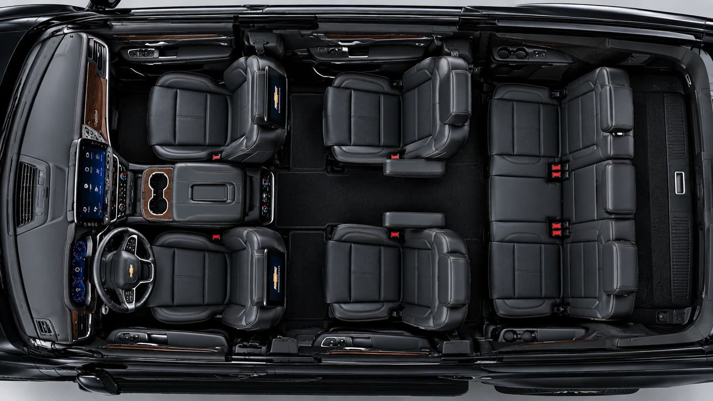 Overhead angle of a Chevrolet Suburban interior showing three rows of black leather seats, dashboard screens, and center console.