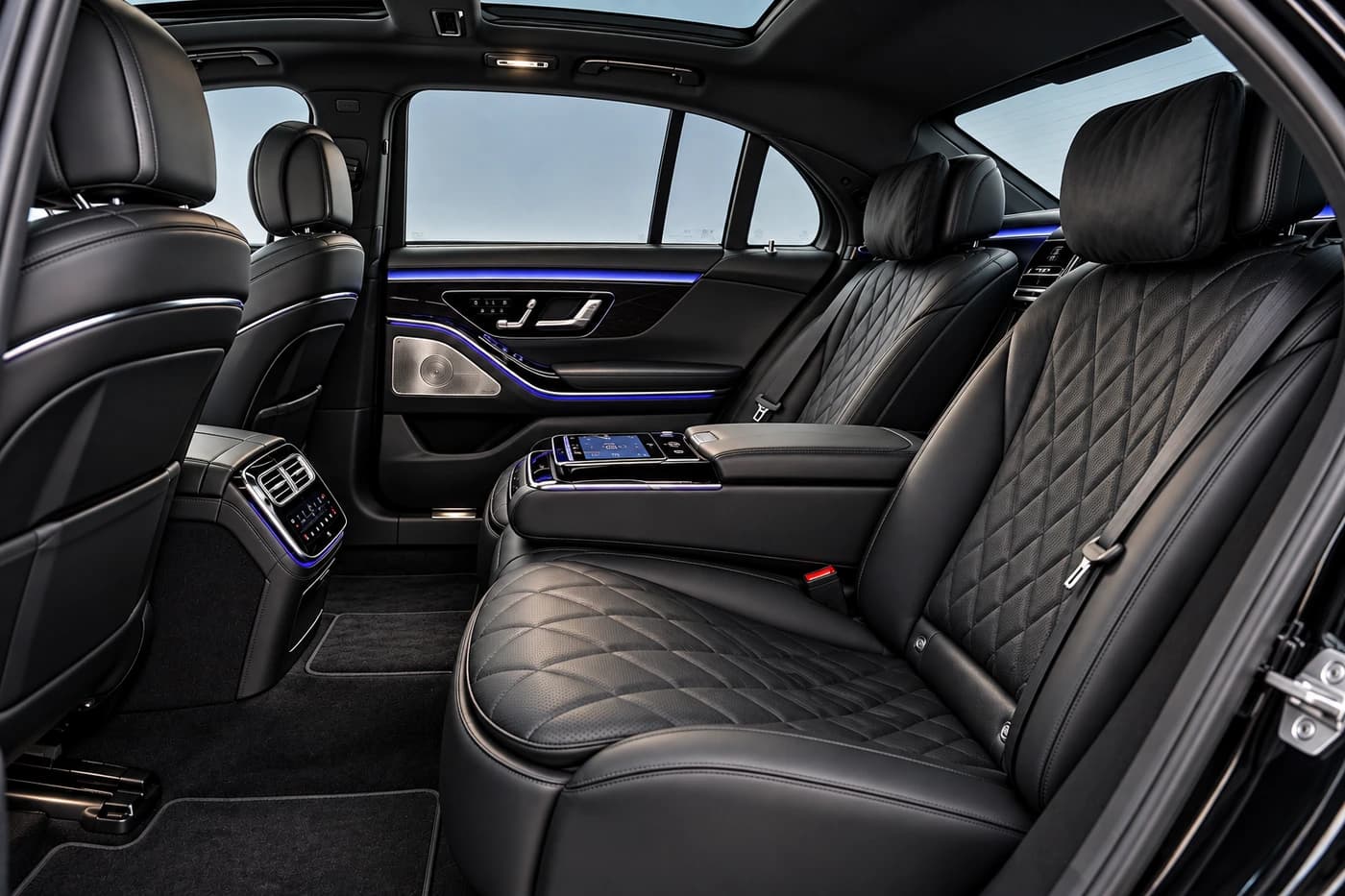 Mercedes-Benz S-Class rear seats in diamond-quilted black leather with a touchscreen armrest and blue ambient lighting.