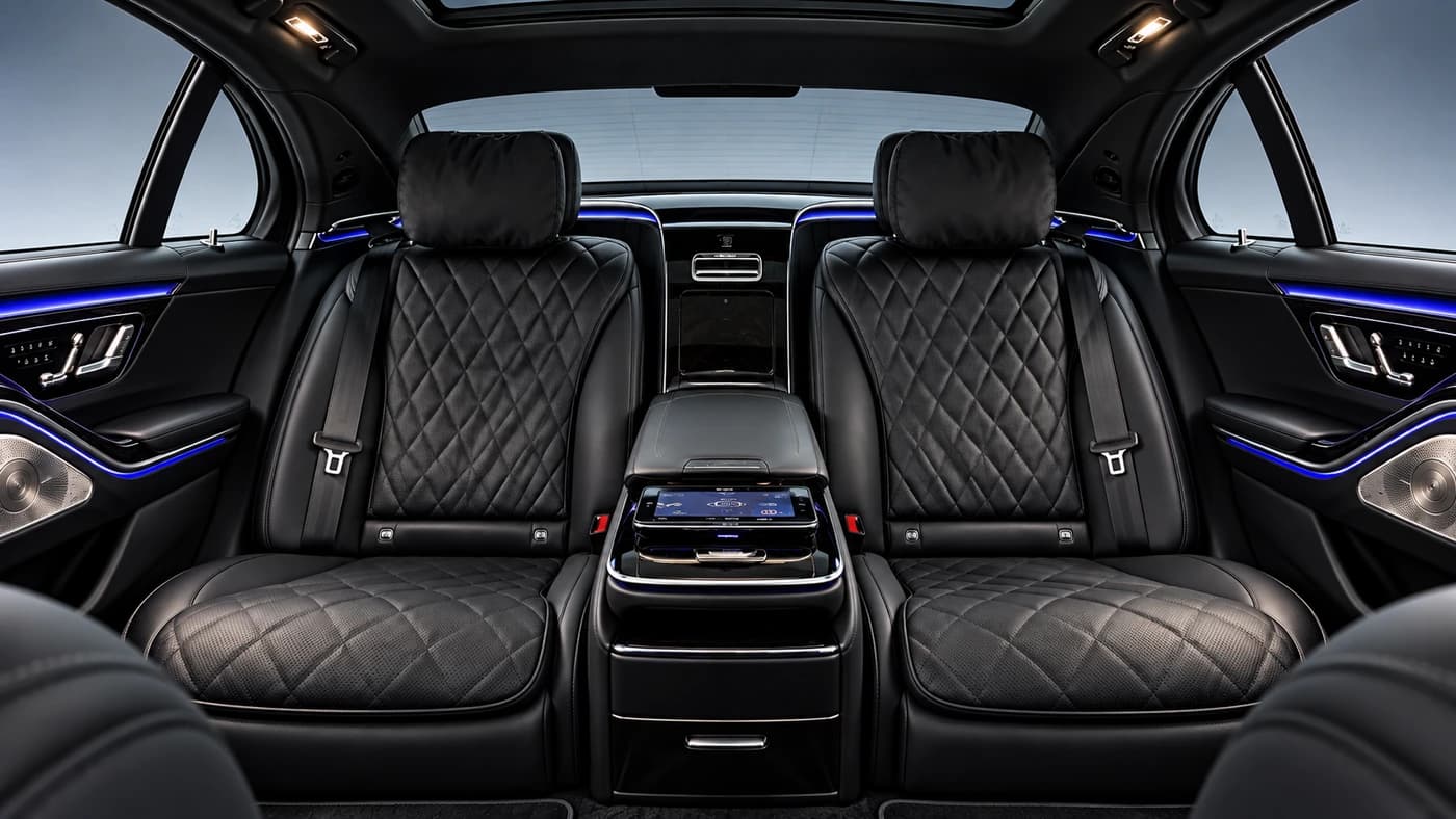 Mercedes-Benz S-Class interior with black quilted leather seats, blue ambient lighting and a center console screen.