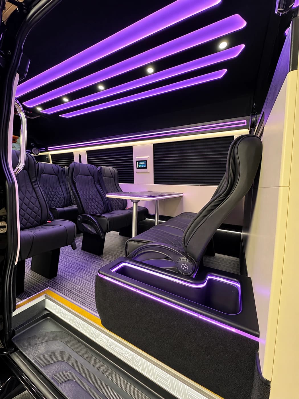 Mercedes-Benz Executive Sprinter cabin with quilted black leather captain's chairs, a table and purple LED ceiling lights.
