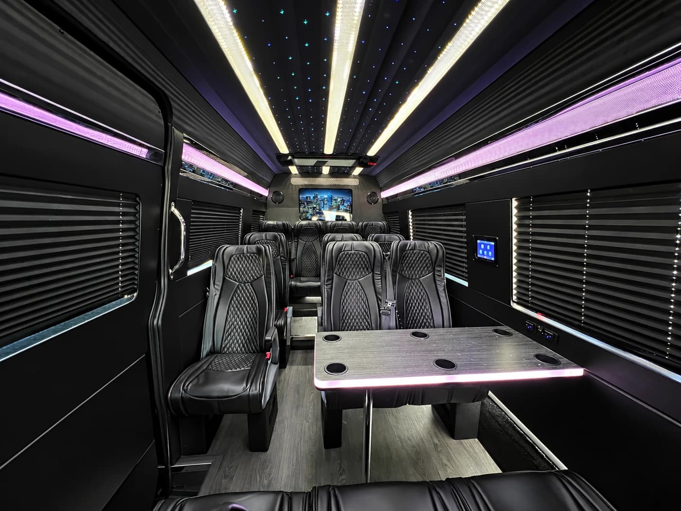Mercedes-Benz Executive Sprinter cabin with black leather seats, a table, a TV screen and LED lighting.