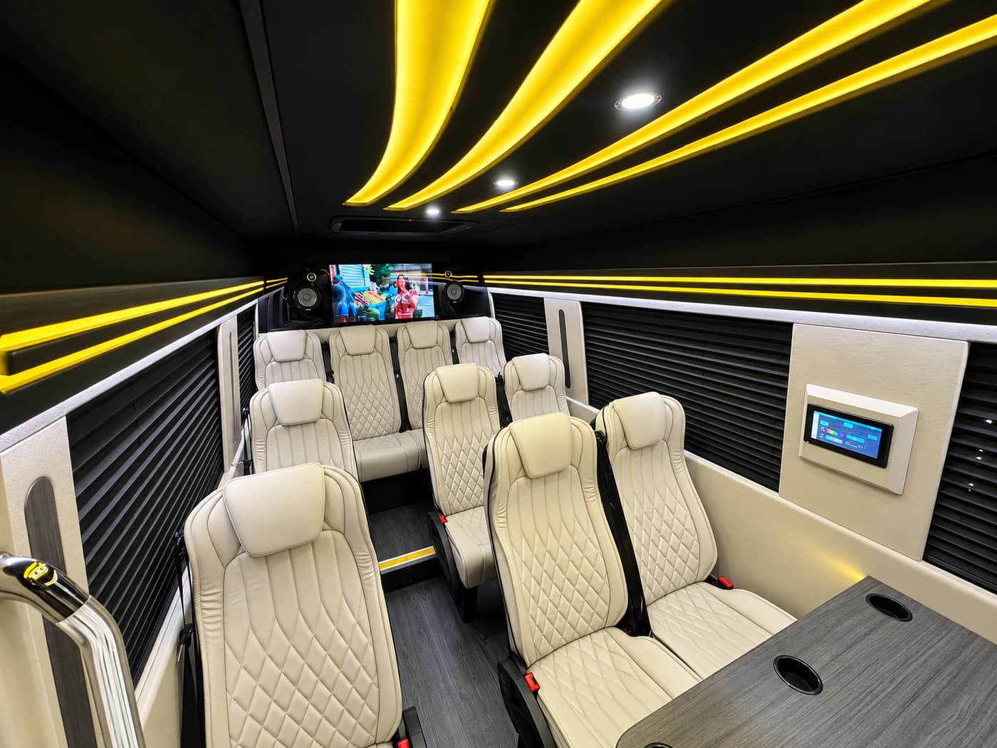 Mercedes-Benz Executive Sprinter interior showing cream leather seats, yellow LED lighting, a rear TV screen, and wall controls.
