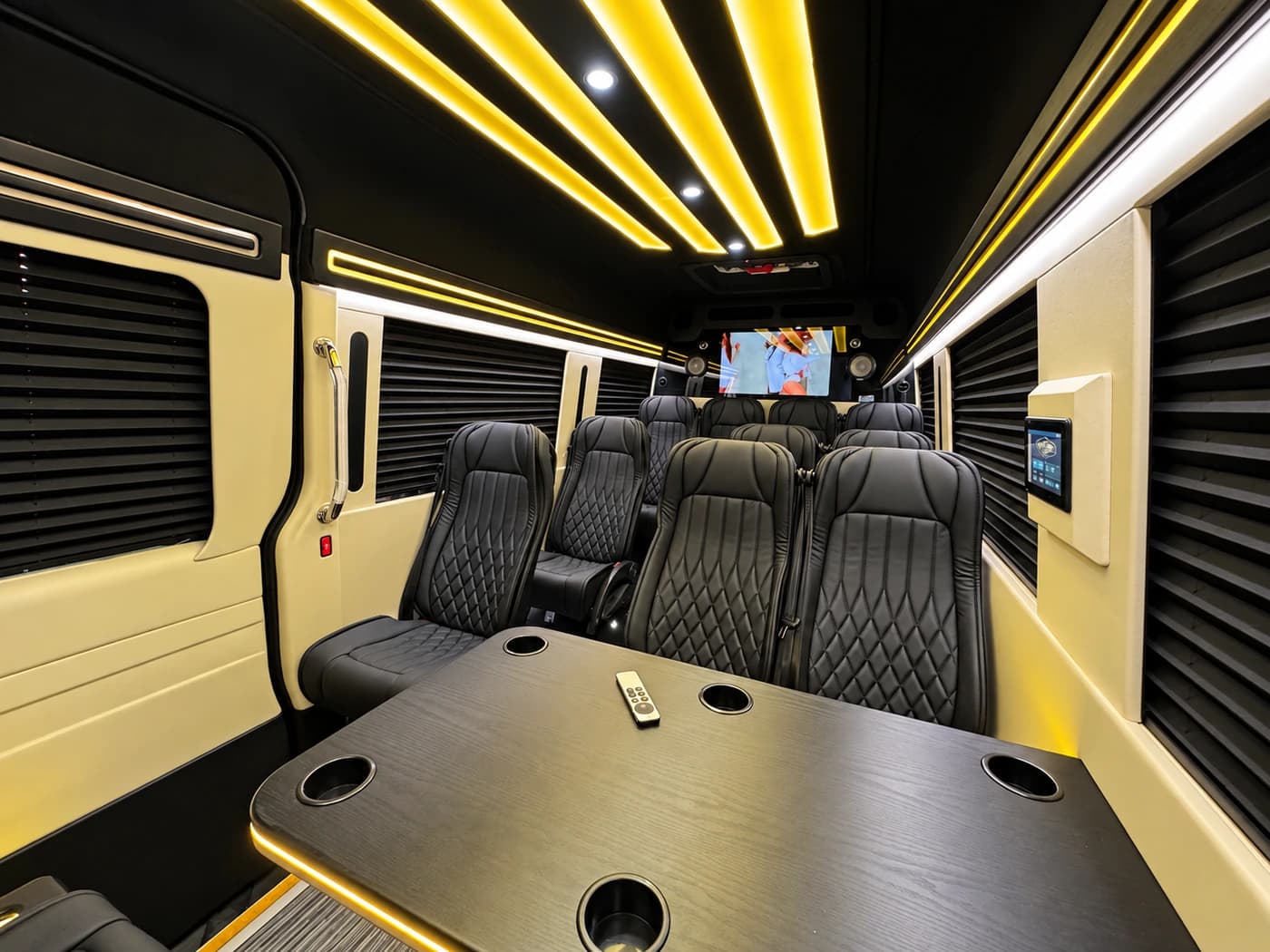 Mercedes-Benz Executive Sprinter cabin with diamond-stitched black leather seats, a table with cupholders, gold LED ceiling lights and a TV.