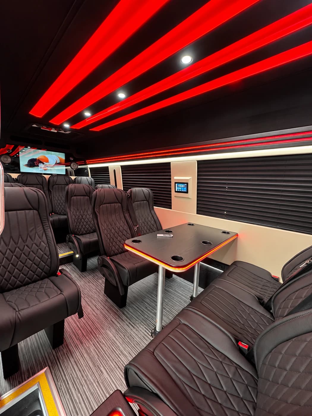 The Mercedes-Benz Executive Sprinter interior shows dark leather seats, a central table, red ceiling lights, and wall screens.