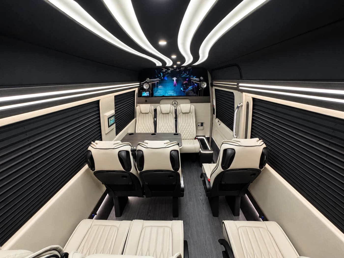 Mercedes-Benz Executive Sprinter cabin with cream leather seats, dark walls, ceiling lights and a screen.