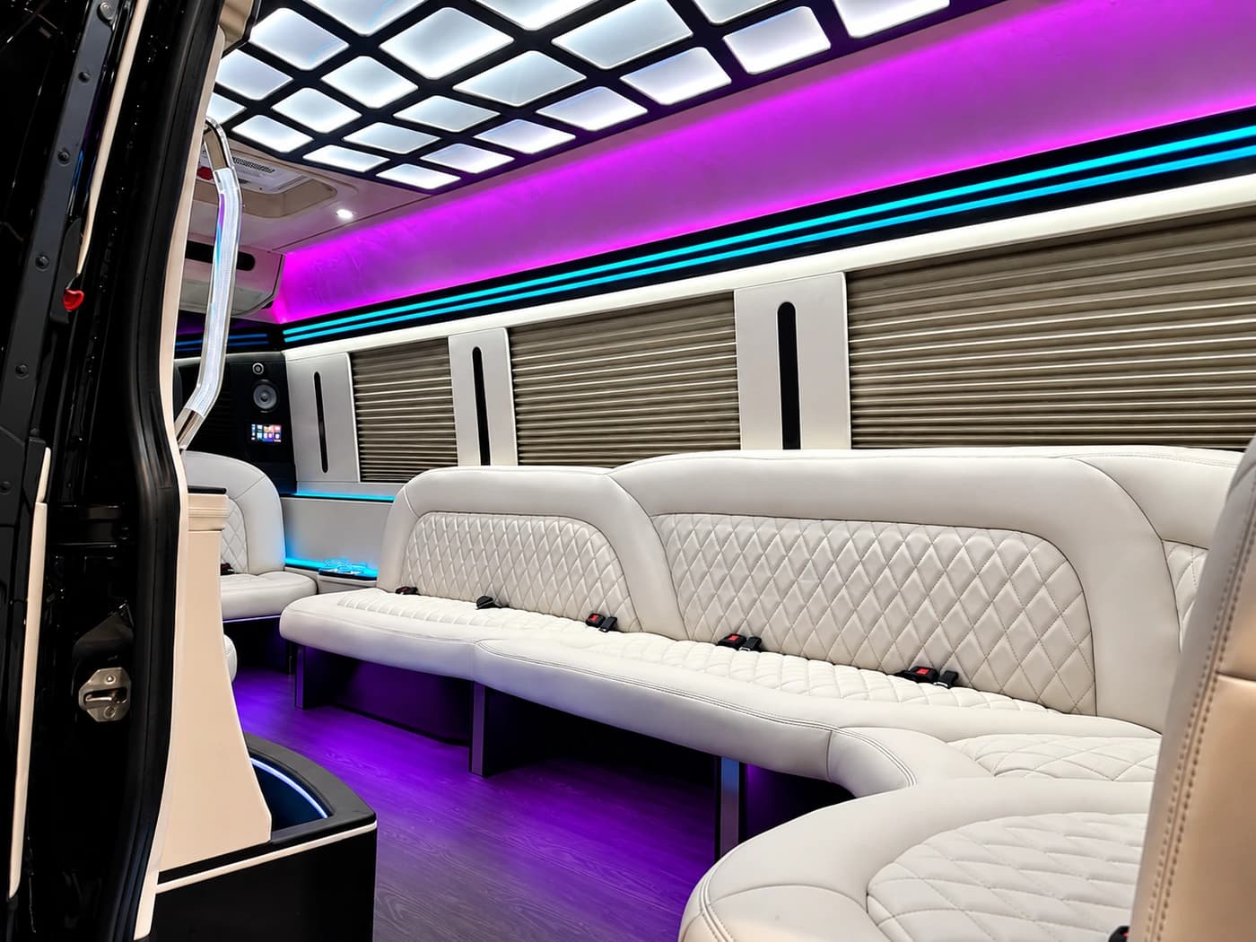 Mercedes-Benz Sprinter limousine interior shows white leather seating, purple LED lighting, wooden flooring, and a side bar counter.